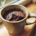 A rich, dark chocolate Single Serve Protein Brownie baked directly in a speckled ceramic mug, resting on a wooden surface.