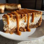 A close-up of a slice of creamy biscoff cheesecake topped with thick caramel sauce dripping down the sides.