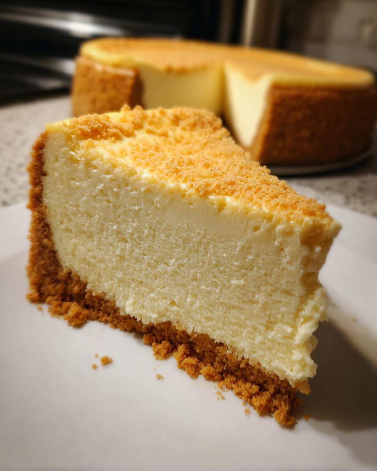 A close-up slice of creamy cheesecake recipe on a white plate with a thick graham cracker crust.