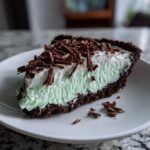 A close-up of a slice of grasshopper pie featuring a dark chocolate crust, light green filling, and topped with chocolate shavings.