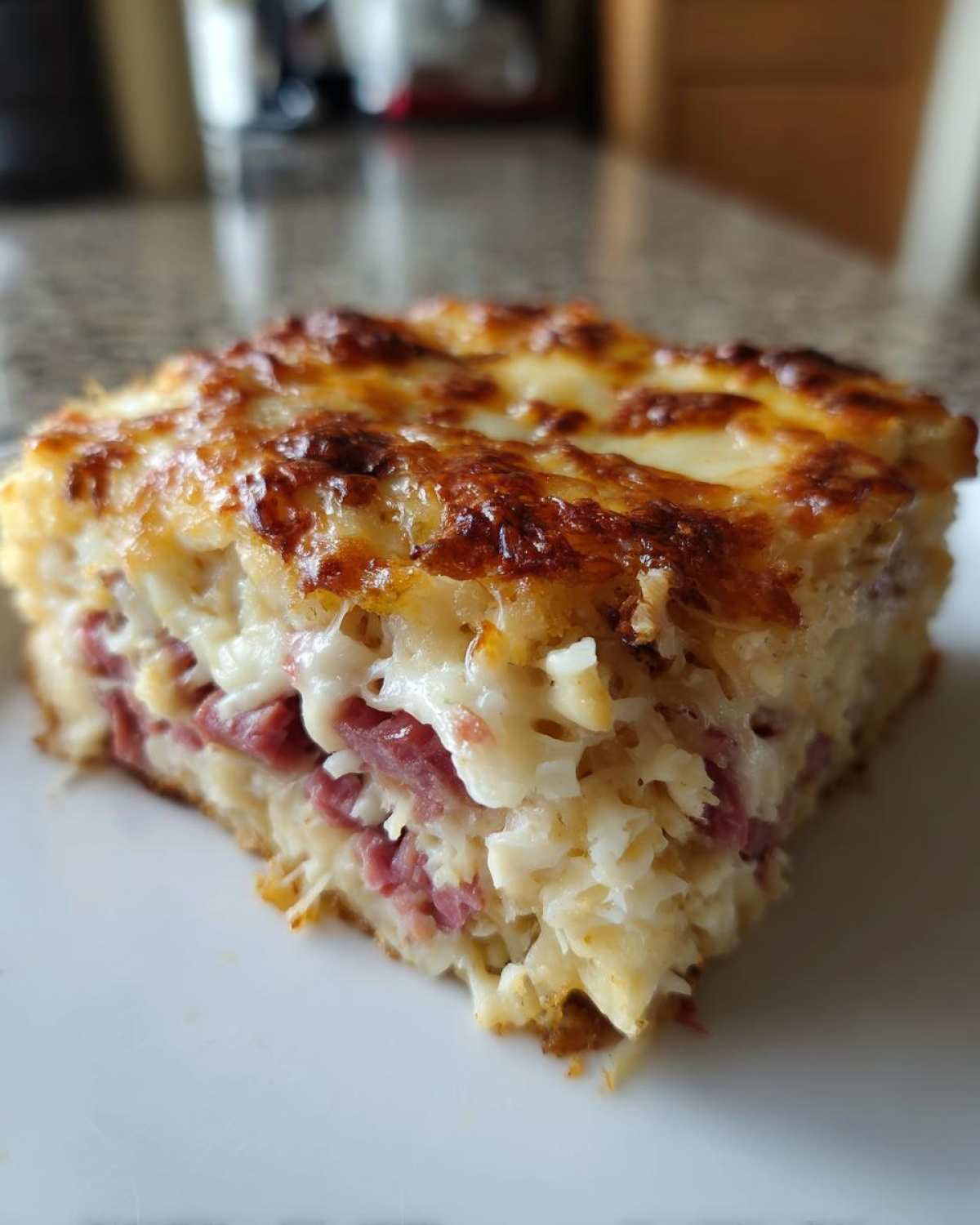 Close-up of a square slice of homemade Reuben bake showing layers of corned beef, sauerkraut, and melted cheese topping.