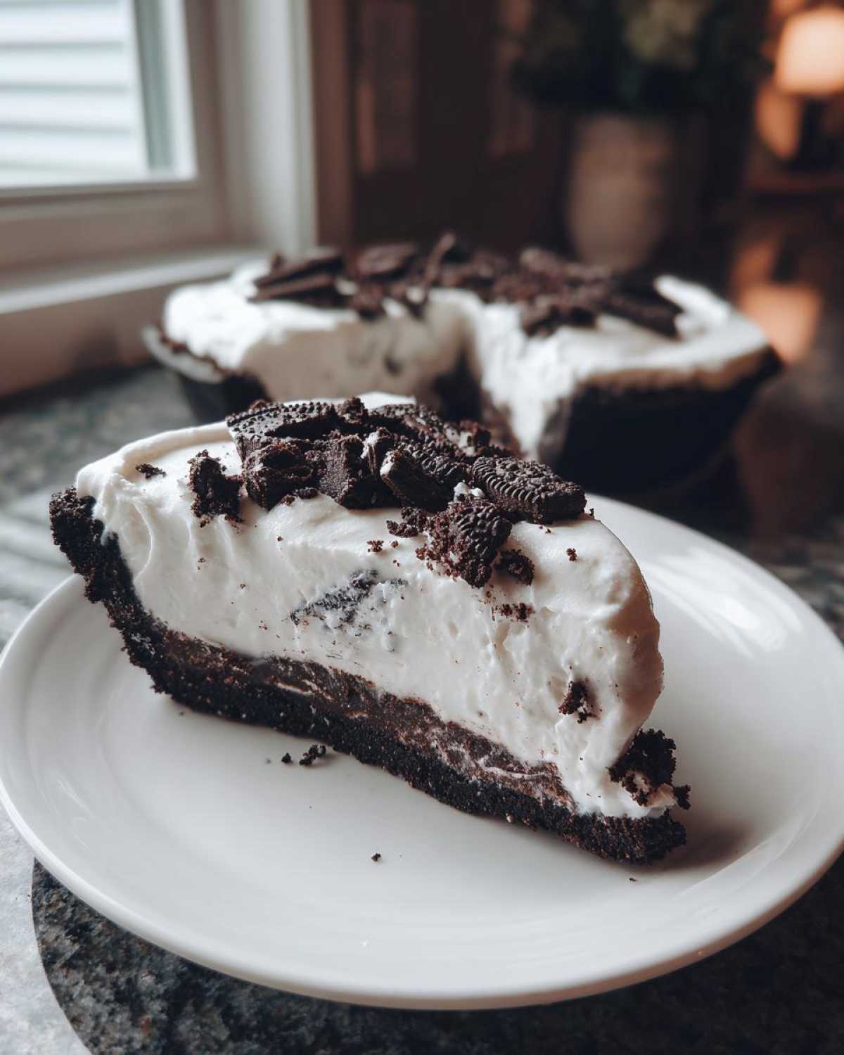 A generous slice of no bake Oreo pie featuring a dark crust, creamy white filling, and crushed Oreo topping on a white plate.