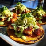 Four vibrant Smash Chicken Tacos on a plate, topped with shredded cabbage and a bright green sauce.