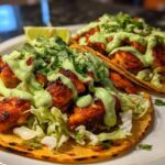 Two delicious Smash Chicken Tacos topped with seasoned chicken, shredded lettuce, creamy green sauce, and cilantro.
