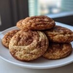 A stack of freshly baked, soft snickerdoodles coated in cinnamon sugar, resting on a white plate.