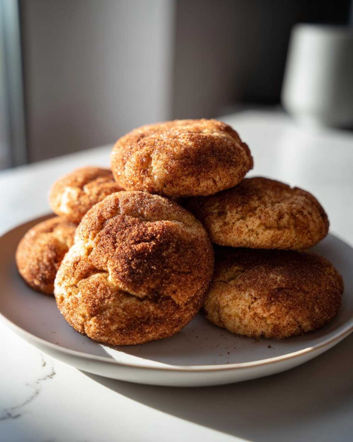 A stack of freshly baked, soft snickerdoodles cookies generously coated in cinnamon sugar on a light gray plate.
