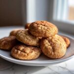 A stack of freshly baked, soft snickerdoodles generously coated in cinnamon sugar, resting on a white plate.