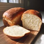 Two golden-crusted loaves of soft sourdough sandwich bread, one sliced to show the fluffy interior.