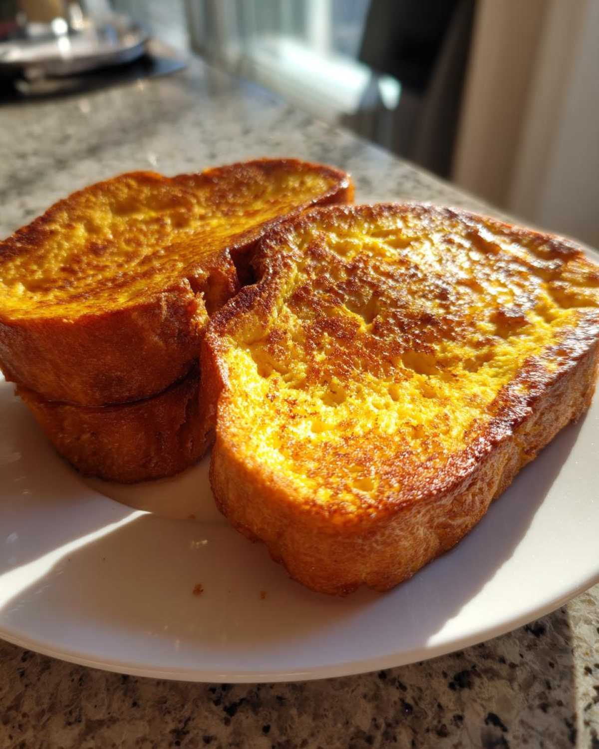 Three thick slices of golden brown sourdough french toast stacked slightly on a white plate.