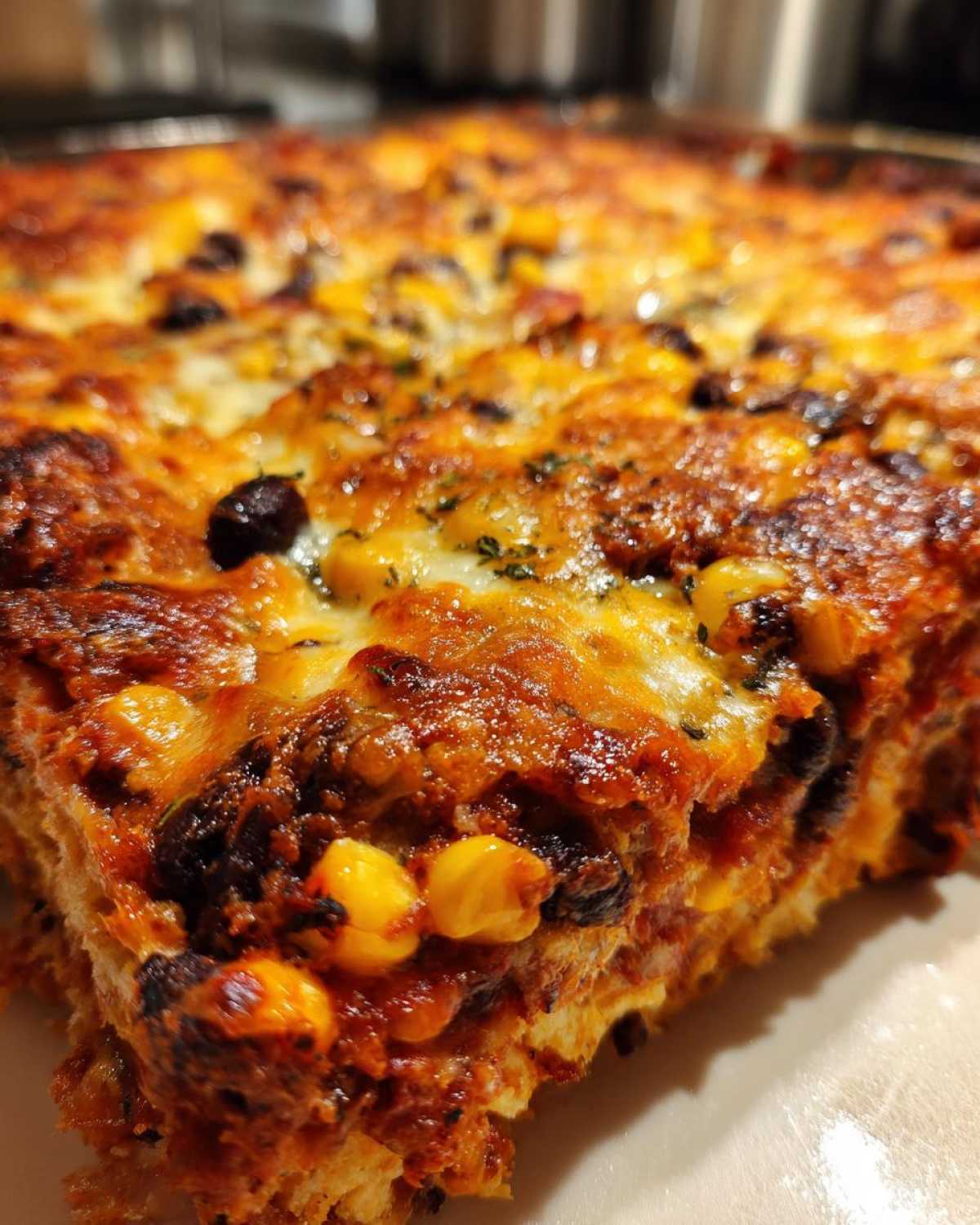 A close-up, macro shot of a slice of Southwestern Black Bean Casserole showing melted, browned cheese, black beans, and corn.