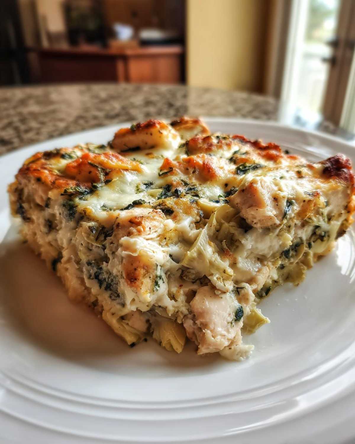 A close-up serving of creamy Spinach Artichoke Chicken Casserole topped with golden, melted cheese on a white plate.