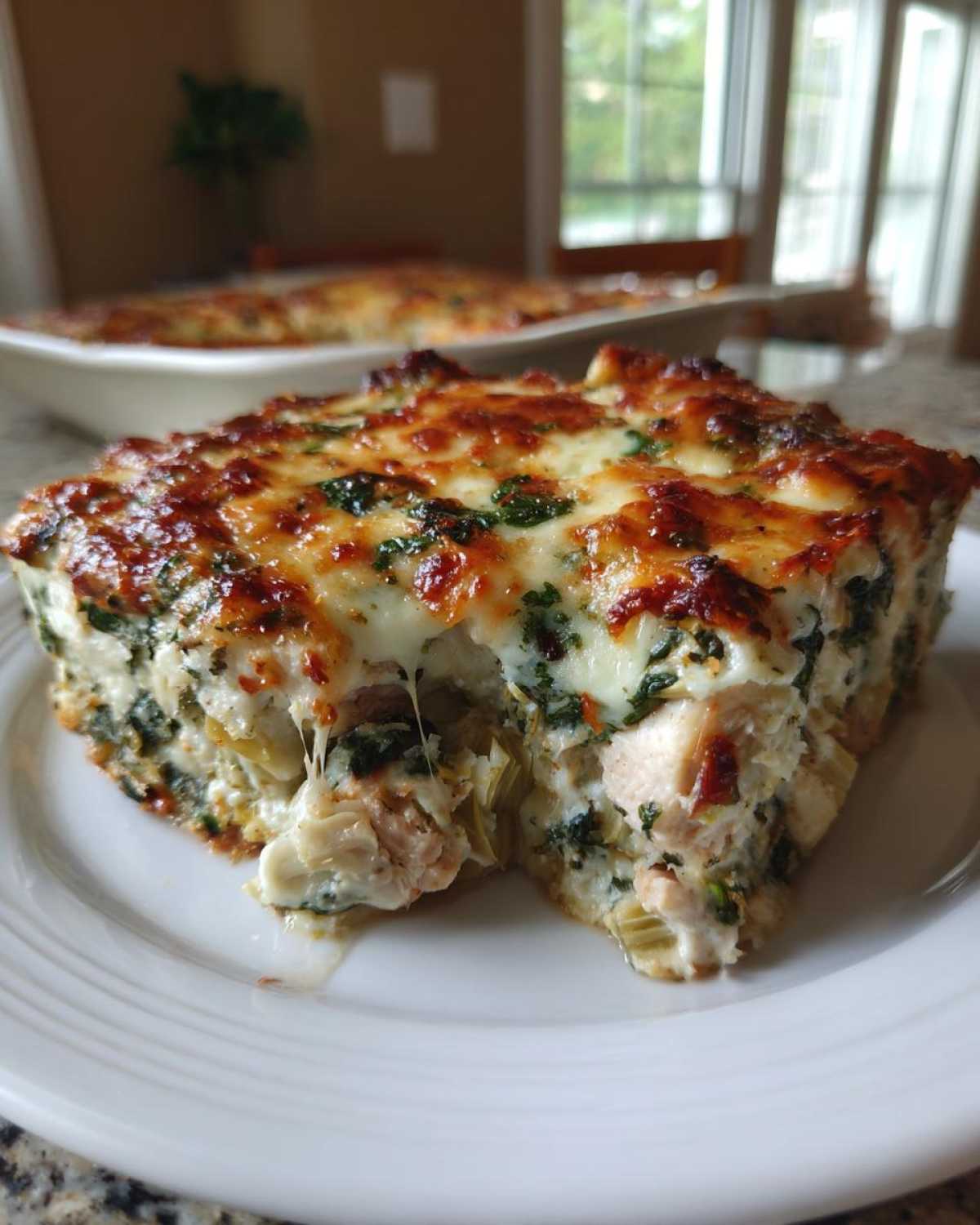 A square slice of cheesy Spinach Artichoke Chicken Casserole with melted, browned topping on a white plate.
