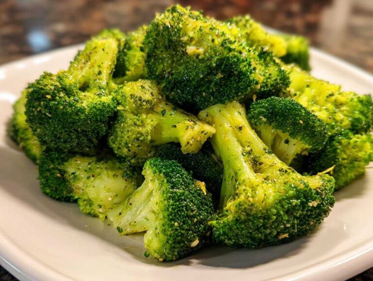 Close-up of bright green, seasoned steamed broccoli florets piled high on a white plate.
