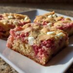 Three squares of rich Strawberry Blondies One Bowl recipe featuring bright pink strawberry filling and white chocolate chips on a white plate.