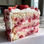 Close-up of a moist slice of strawberry cake showing layers of white cake, strawberry filling, and whipped cream frosting.