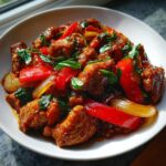 A close-up shot of glistening Sweet Spicy Thai Chicken pieces mixed with red bell peppers, onions, and fresh basil leaves in a white bowl.