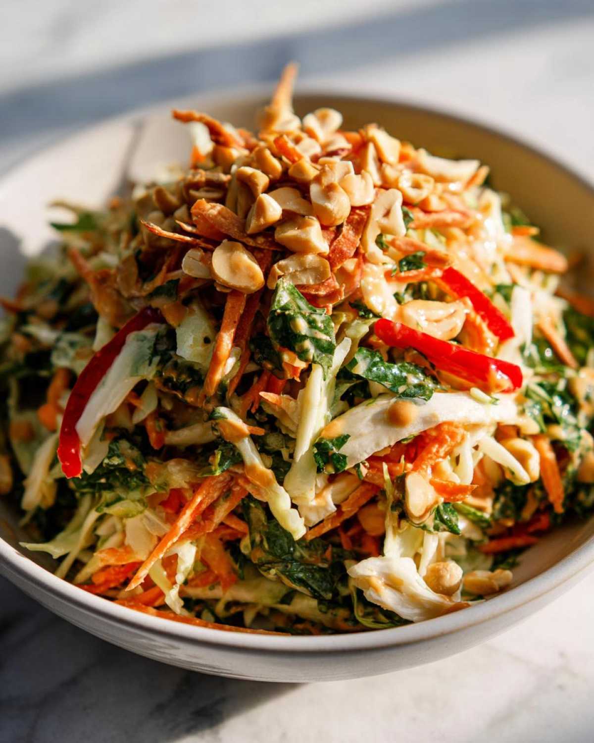 A vibrant bowl of thai chicken salad featuring shredded cabbage, carrots, red pepper, and topped generously with chopped peanuts.