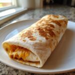 A golden-toasted Vegetarian Bean Cheese Burrito showing melted cheddar cheese spilling out slightly.