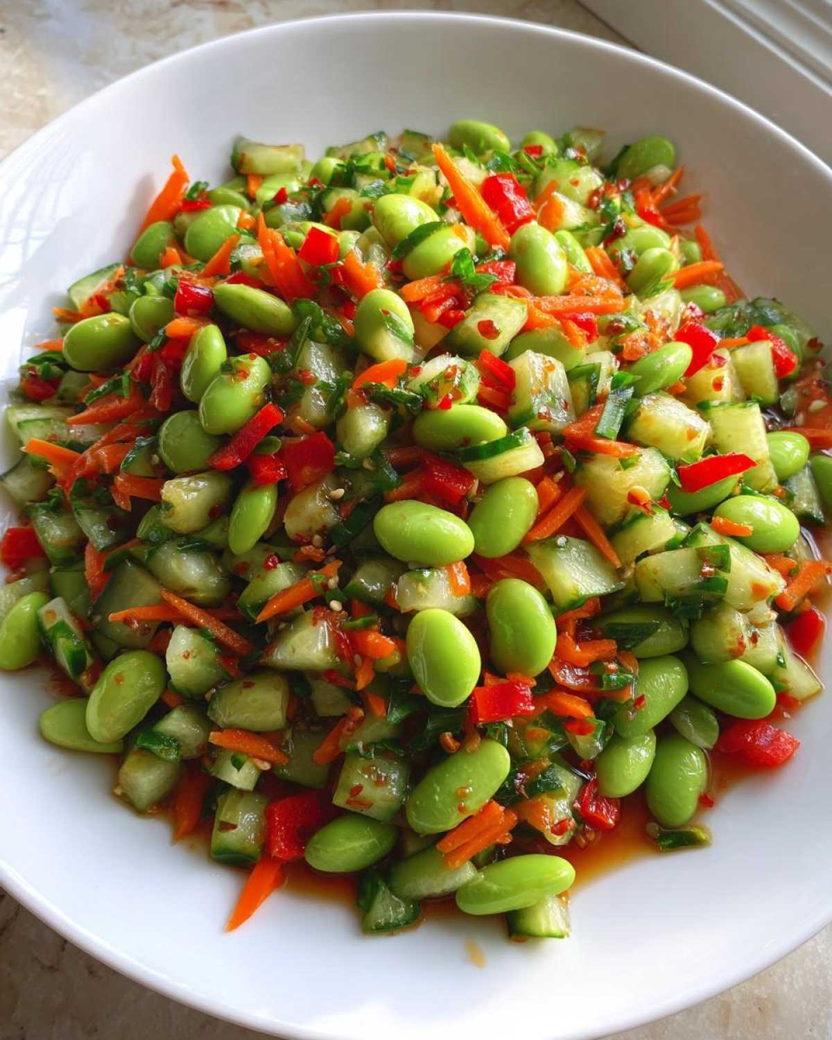 Close-up of a vibrant, colorful edamame salad featuring bright green edamame, diced cucumbers, shredded carrots, and red peppers.