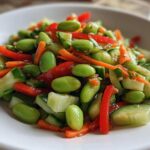 Close-up of a bright, fresh edamame salad featuring shelled edamame, sliced cucumber, julienned carrots, and red bell pepper.