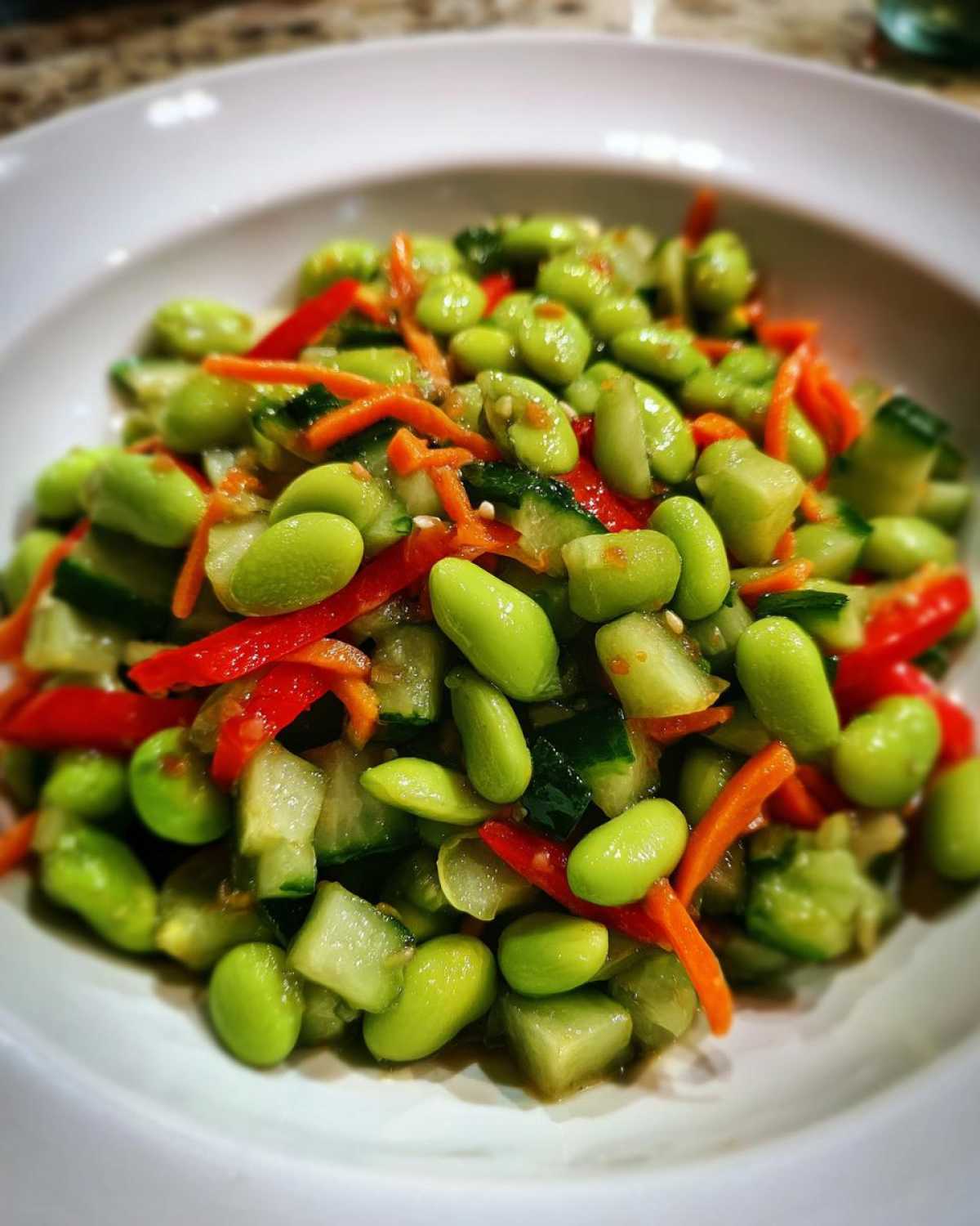 Close-up of a vibrant edamame salad featuring bright green edamame, diced cucumber, shredded carrots, and red pepper strips.