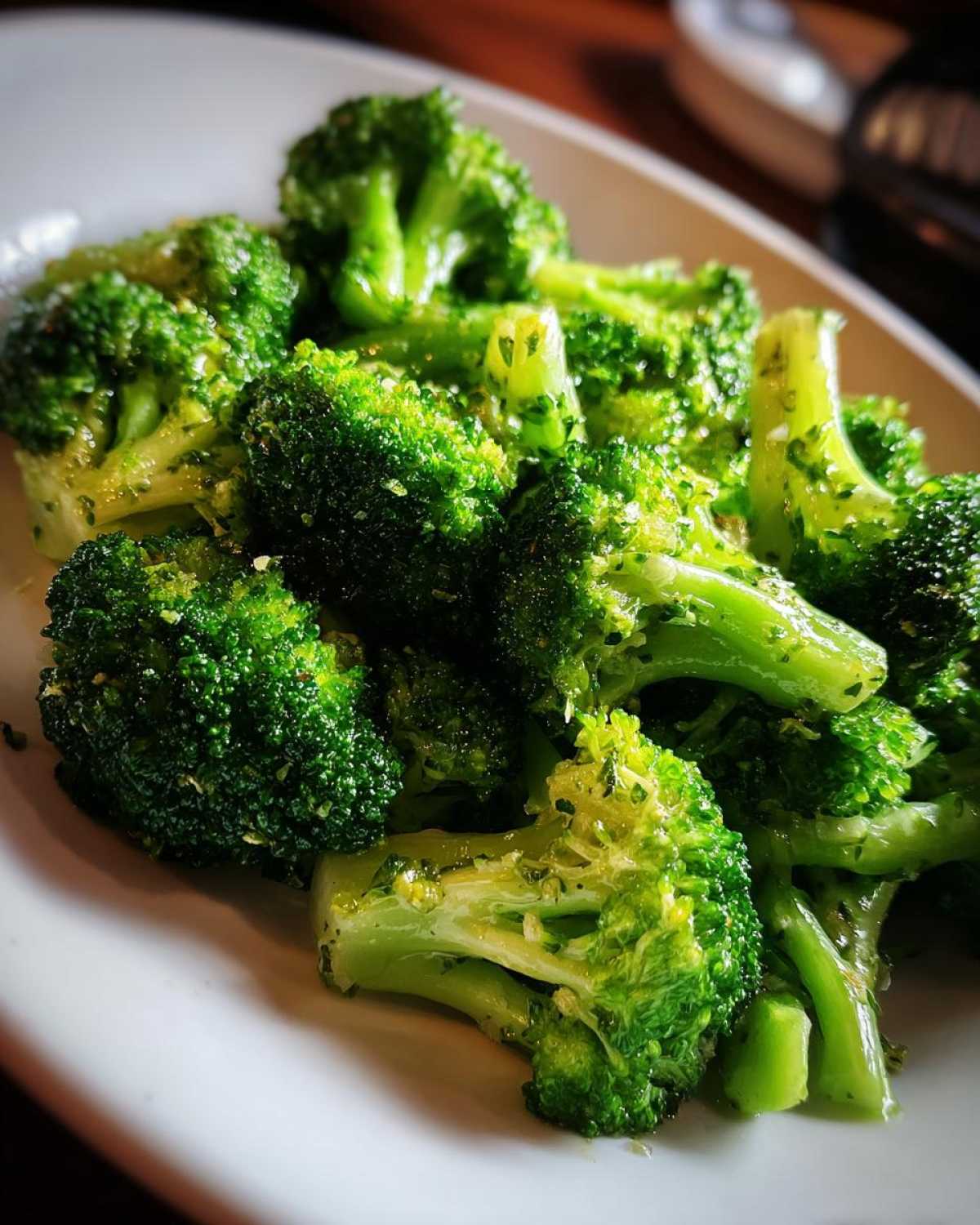 Close-up of perfectly cooked steamed broccoli florets glistening with butter and herbs on a white plate.