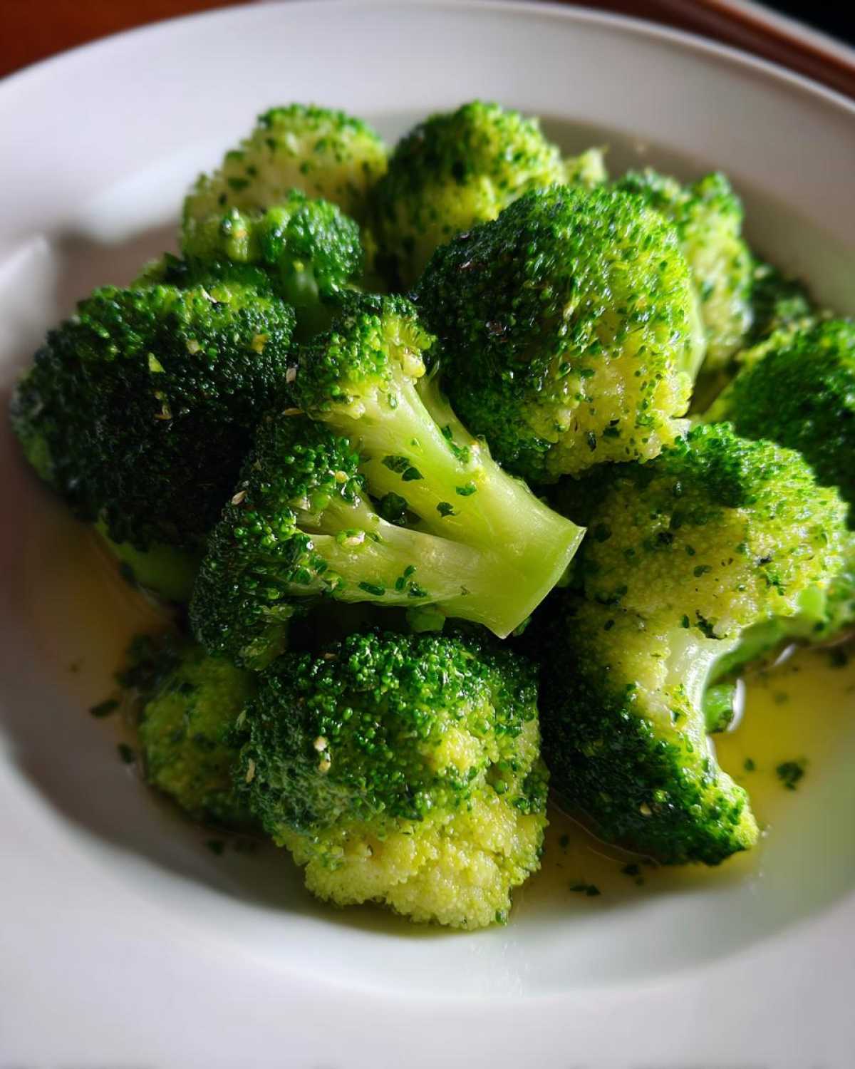 Close-up of vibrant steamed broccoli florets seasoned with herbs and sitting in a light sauce or melted butter.