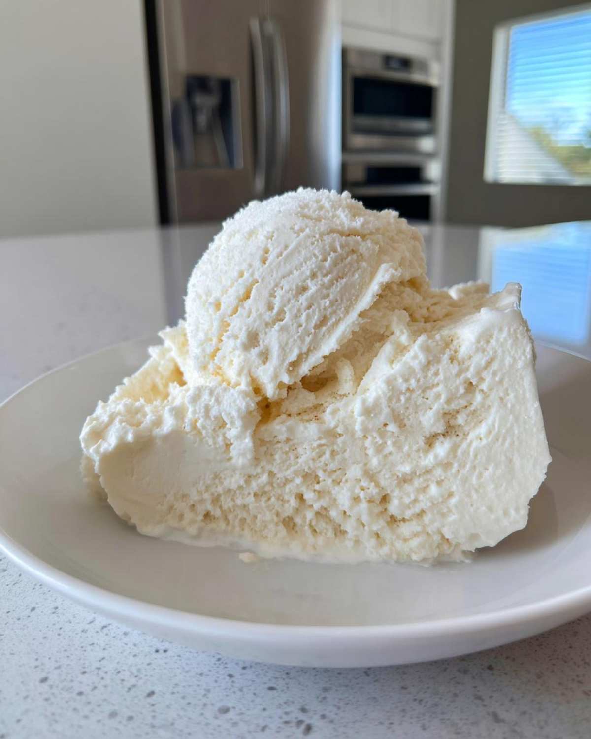 A generous scoop of creamy white cottage cheese ice cream served in a white bowl on a speckled countertop.