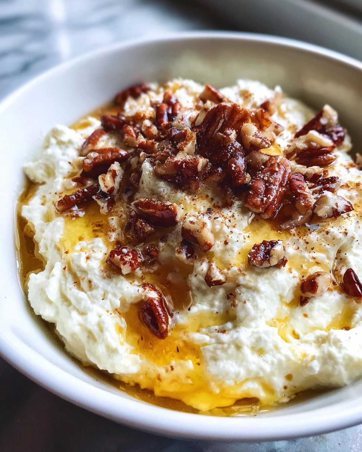 Close-up of creamy whipped goat cheese drizzled with honey and topped with chopped pecans.