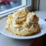 A generous mound of fluffy, pale yellow whipped honey butter recipe sprinkled with cinnamon, served on a white plate.