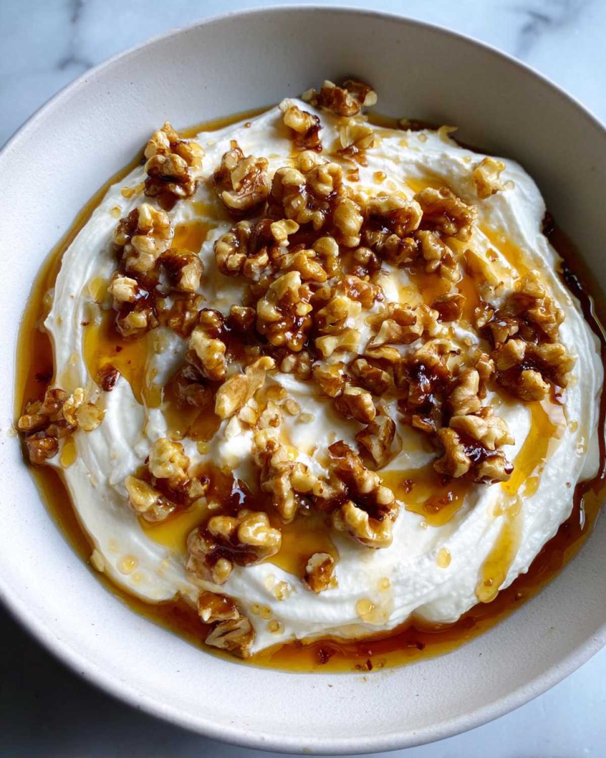 Overhead view of a bowl of creamy whipped ricotta dip drizzled with honey and topped with toasted walnuts.