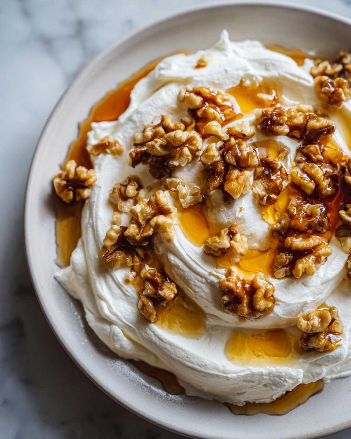 Close-up of a bowl of creamy whipped ricotta dip topped generously with walnuts and drizzled with golden honey.