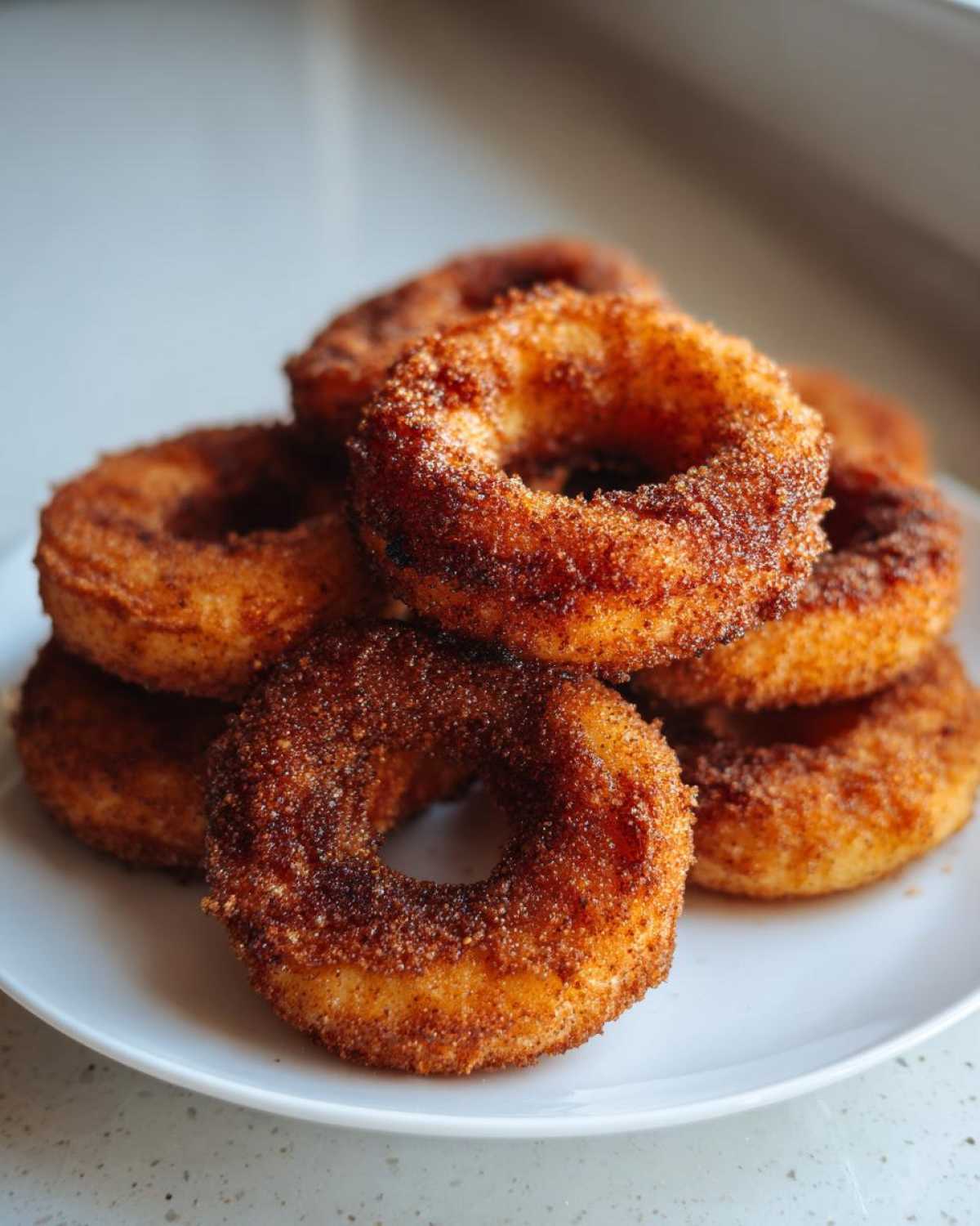A close-up stack of golden brown Air Fryer Cinnamon Apple Rings heavily coated in cinnamon sugar.