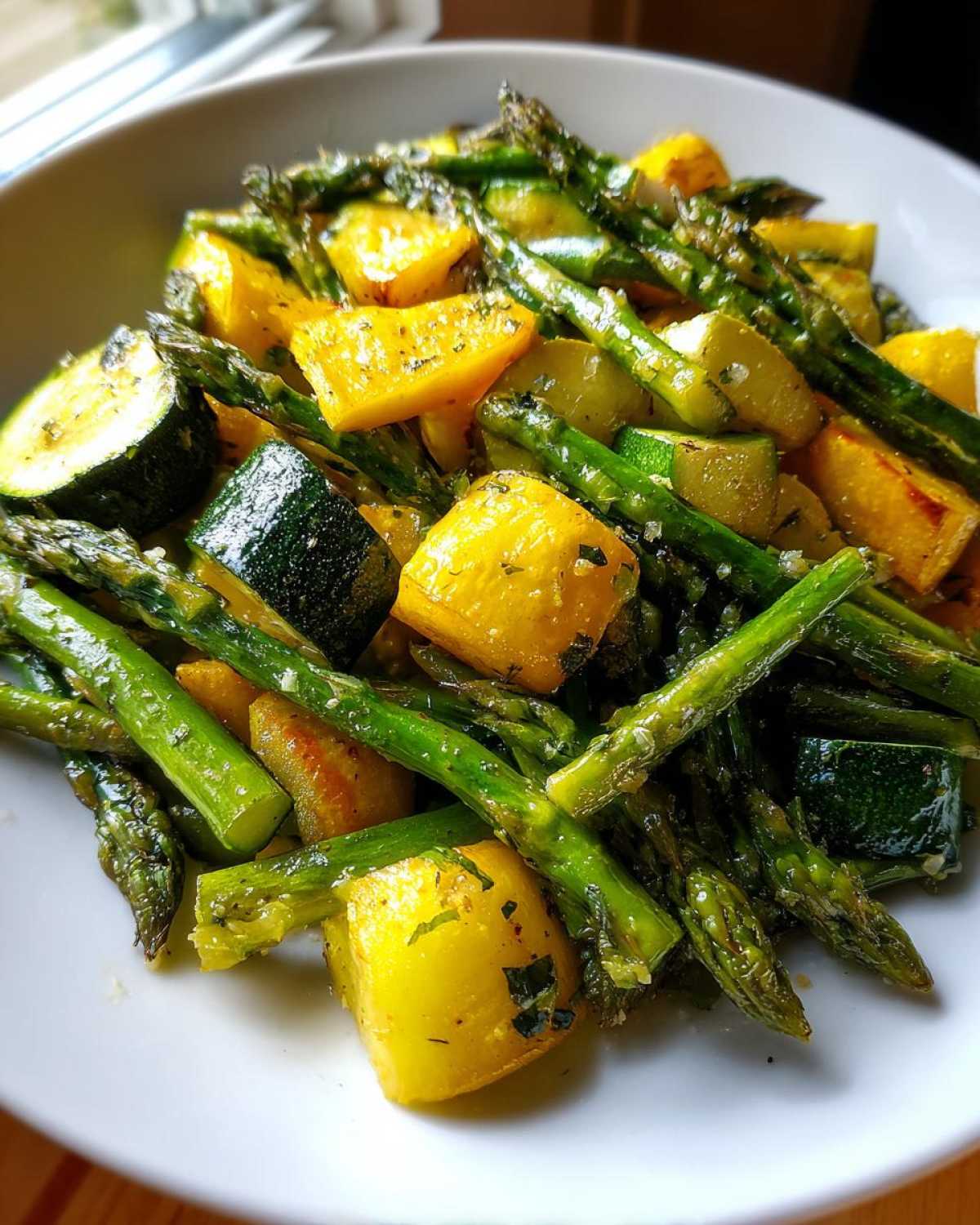 Close-up of sautéed asparagus with zucchini and yellow squash chunks, seasoned with herbs.