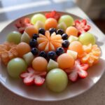 A stunning Baby Bloom Fruit Platter featuring melon balls, blueberries, and strawberries cut into flower shapes.