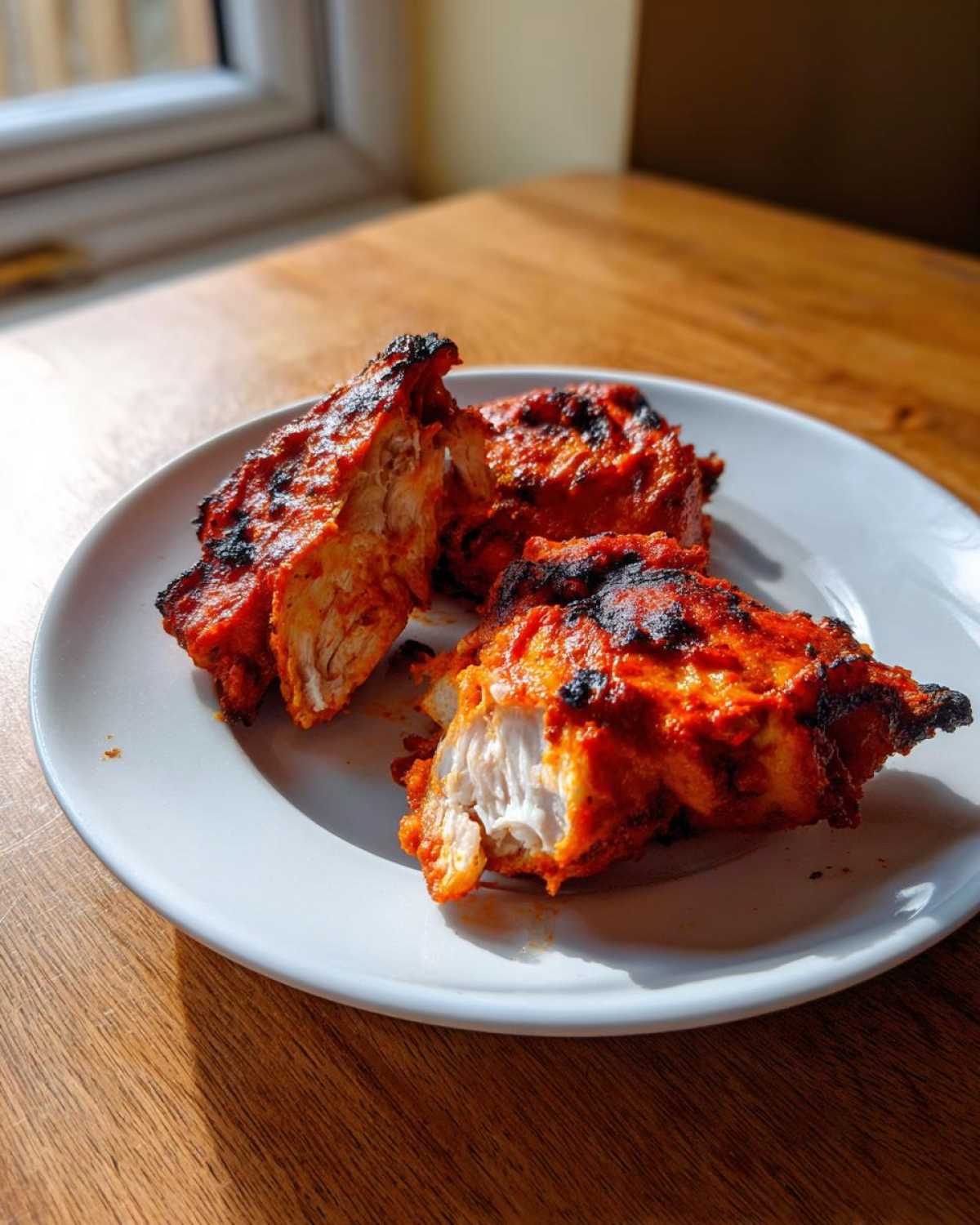 Close-up of three pieces of vibrant red Baked Tandoori Chicken Oven, one piece broken open showing white meat.