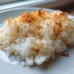 A close-up of a serving of Bobby Flay's Crispy Coconut Rice topped with golden brown toasted coconut flakes.