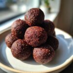 A stack of rich, dark Brownie Protein Bites on a light ceramic plate, showing texture.