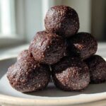A stack of rich, dark Brownie Protein Bites Steps Healthy piled on a light ceramic plate near a window.