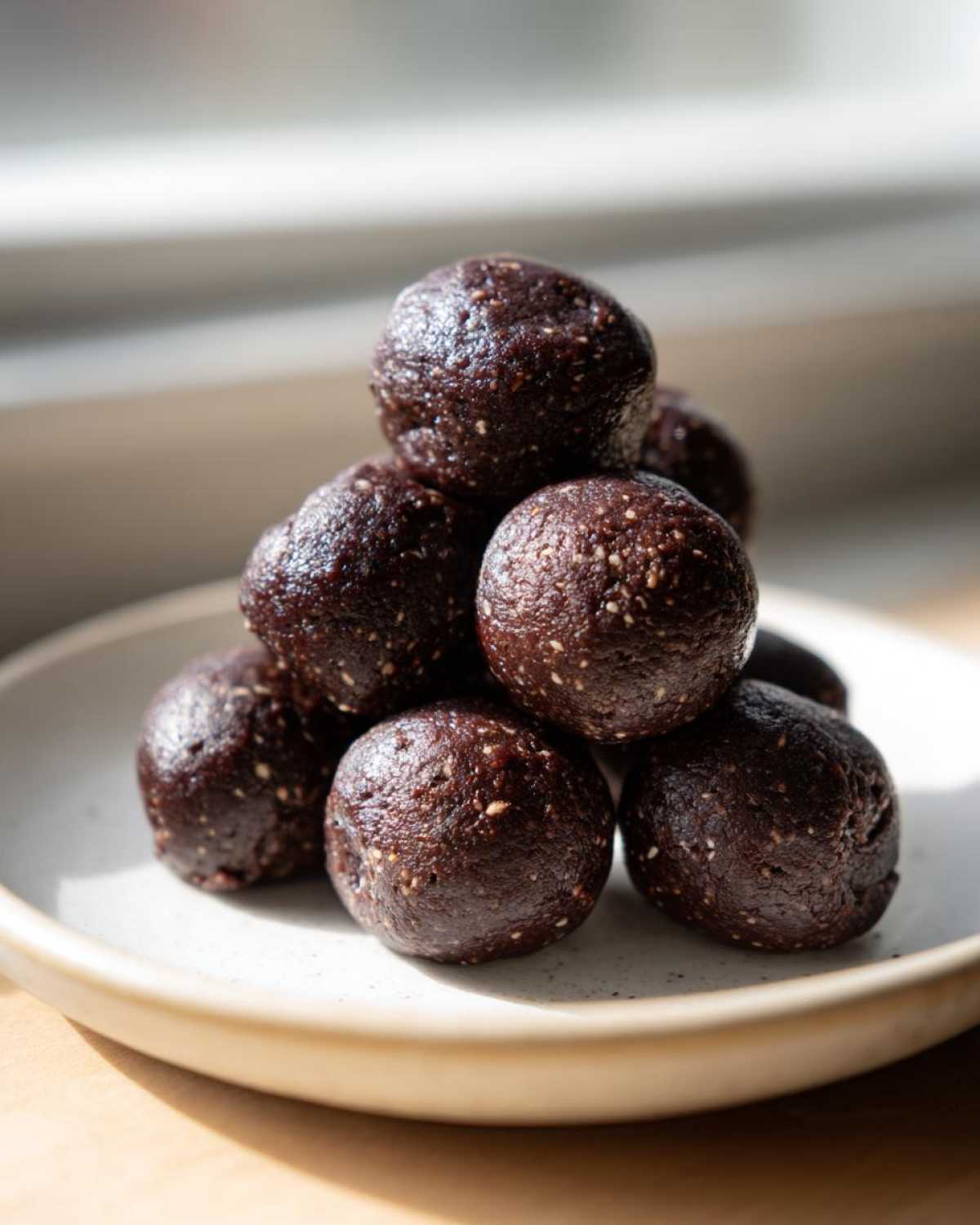 A stack of dark, rich Brownie Protein Bites Steps Healthy on a light speckled plate, illuminated by natural light.