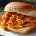 A close-up of a soft bun generously filled with shredded, saucy Buffalo Chicken Crock Pot Sandwiches filling.