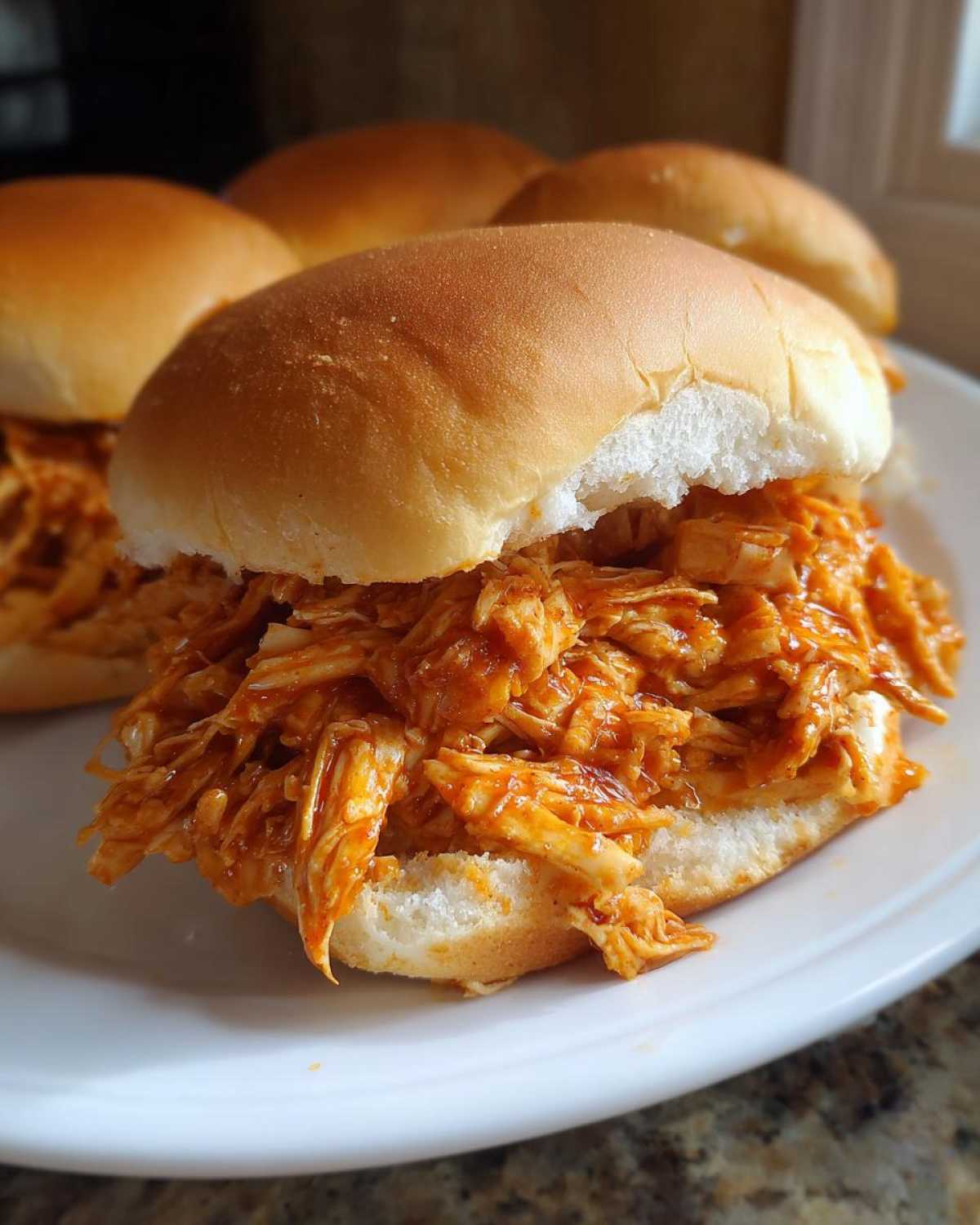 A close-up of one Buffalo Chicken Crock Pot Sandwiches piled high with shredded orange buffalo chicken on a soft white slider bun.