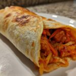 A close-up of a perfectly rolled Chili Chicken Wraps Lunch showing spicy chicken and shredded vegetables inside a toasted tortilla.