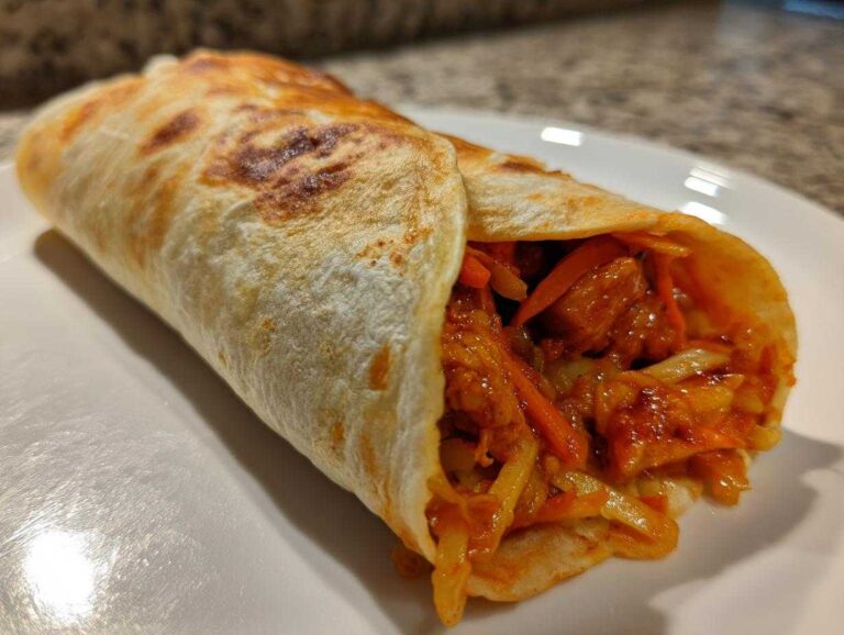 A close-up of a perfectly rolled Chili Chicken Wraps Lunch showing spicy chicken and shredded vegetables inside a toasted tortilla.
