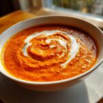 Close-up of rich orange Creamy Garlic Tikka Masala Sauce topped with a white cream swirl in a white bowl.