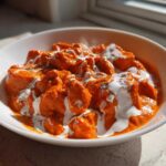 Close-up of rich orange Creamy Garlic Tikka Masala Sauce with chicken pieces, drizzled with white cream.