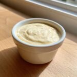 A small white ramekin filled with thick, creamy Hot Honey Ranch Sauce, speckled with spices, sitting on a wooden surface.