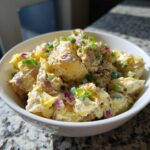 Close-up of creamy Jamaican Jerk Potato Salad mixed with red onion and topped with green onions in a white bowl.