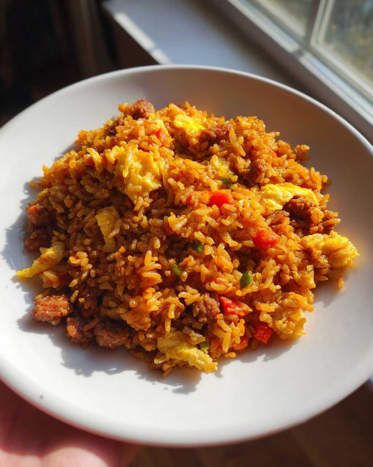 A close-up of vibrant Creole Garlic Fried Rice with scrambled egg and sausage served in a white bowl.
