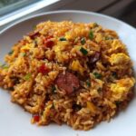 A close-up of vibrant Creole Garlic Fried Rice mixed with sliced sausage and scrambled egg on a white plate.
